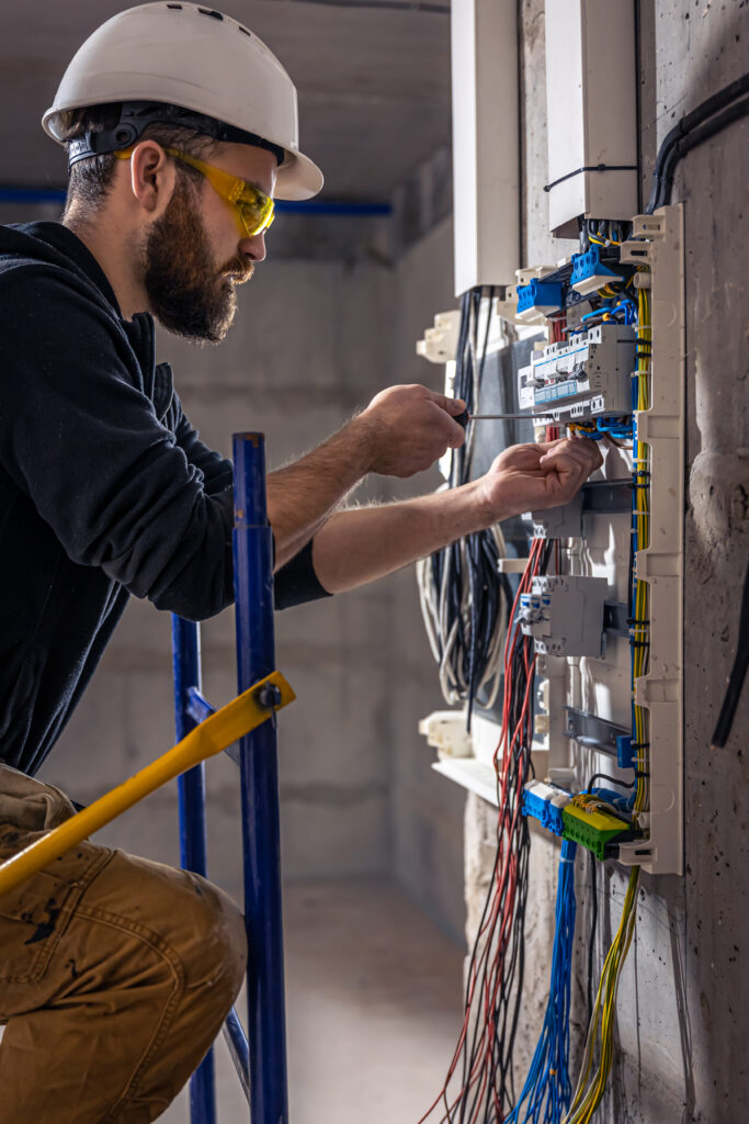 a male electrician works in a switchboard with an electrical connecting cable. a male electrician works in a switchboard with an electrical connecting cable.